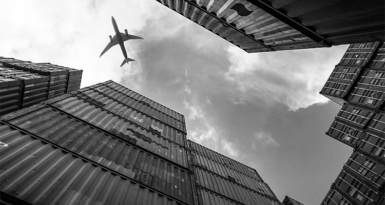 an airplane in the sky above large stacks of intermodal shipping containers