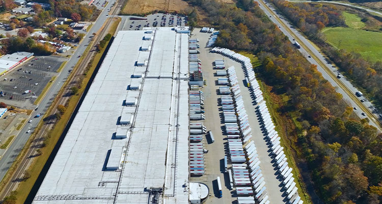 an aerial view of a large warehouse or distribution center with numerous semi-truck trailers parked in rows